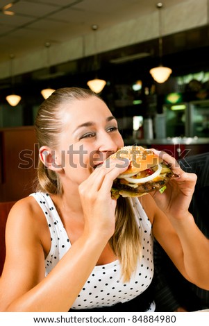 Happy woman in a fast food restaurant eating a hamburger and seems to enjoy it