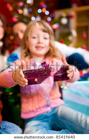 Christmas - happy family (parents with daughter) with gifts on Xmas Eve; focus on gift in front