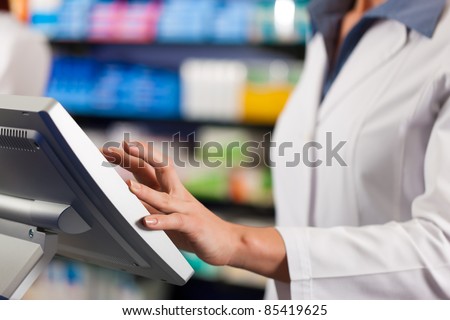 Female pharmacist standing at the cashier in pharmacy, only torso to be seen