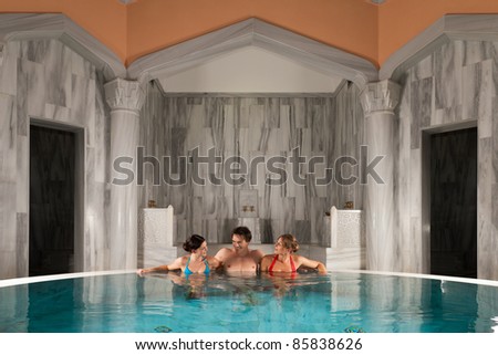 Three friends - one man and two women - in swimming pool or thermal bath doing wellness