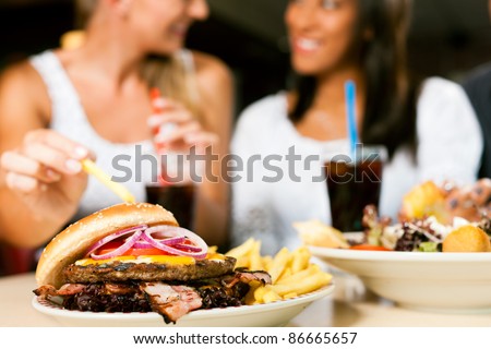 Two women - one is African American - eating hamburger and drinking soda in a fast food diner; focus on the meal