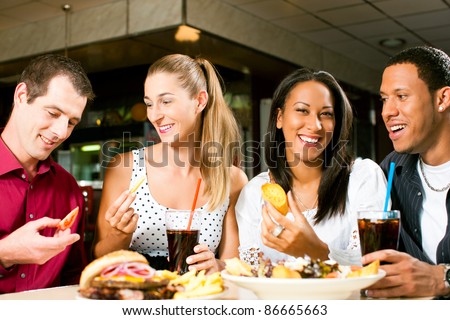 Friends - one couple is African American - eating hamburger and drinking soda in a fast food diner; focus on the meal