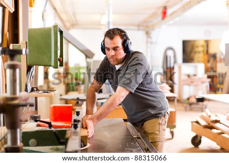 Carpenter is standing on electric cutter with ear protection