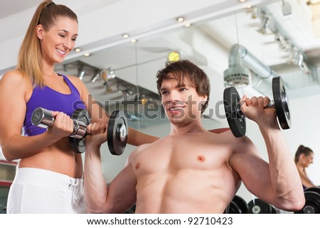 Young fitness couple exercising in gym with weights, one of them is personal trainer