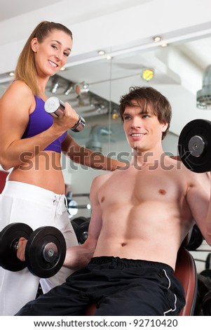 Young fitness couple exercising in gym with weights, one of them is personal trainer