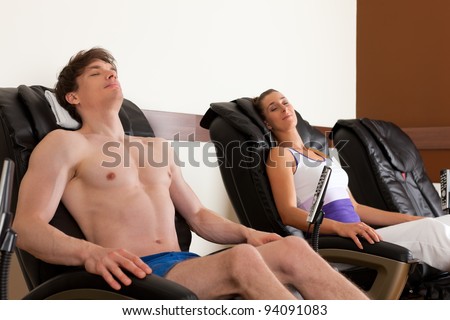 Young couple is recovering on massage chair in gym after exercising for their fitness, the woman is holding the remote control for the chair