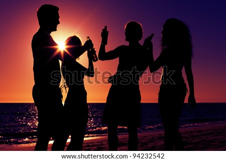 People (two couples) on the beach having party, drinking and having a lot of fun in the sunset (only silhouette of people to be seen, people having bottles in their hands with the sun shining through)