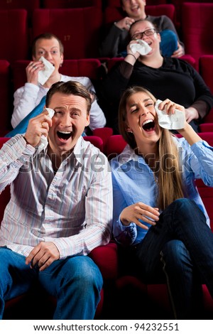 Couple and other people, probably friends, in cinema watching a movie; it seems to be a funny movie