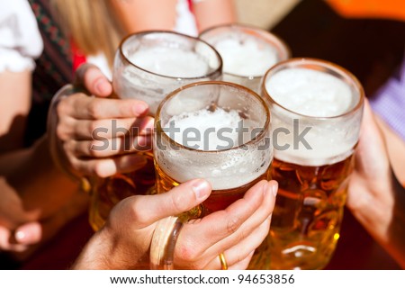Four friends with a fresh beer in a Beer garden close-up on beer stein Four friends with a fresh beer in a Beer garden close-up on beer stein