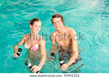 Fitness - a young couple (man and woman) doing sports and gymnastics or water aerobics under water in swimming pool or spa with dumbbells