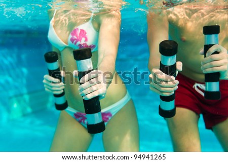 Fitness - a young couple (man and woman) doing sports and gymnastics or water aerobics under water in swimming pool or spa with dumbbells