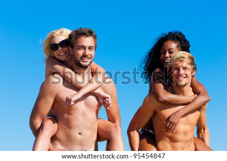 Four friends - men and women - on the beach having lots of fun, the men carrying the women pack back