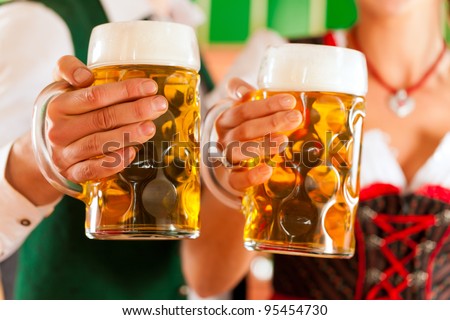 Young man and woman in traditional Tracht with beer glass in brewery, in front of brewing kettle