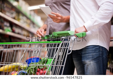 Cropped image of couple shopping groceries together with trolley at supermarket