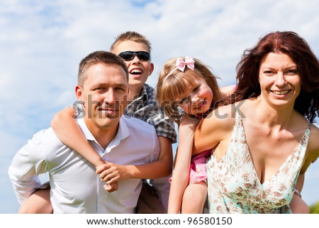 Happy family - mother, father, children - standing on a meadow in summer under blue sky