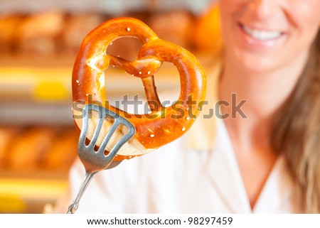 Young salesperson in a bakery is packing bread and pretzels for a customer