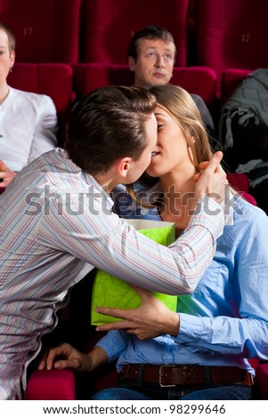 Couple in cinema watching a movie, they eating popcorn and kissing