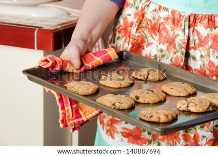 Woman in apron taking hot cookies from oven