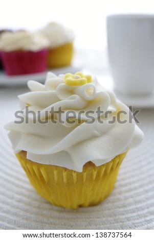 Lemon cupcake with more cakes and coffee cup in the background