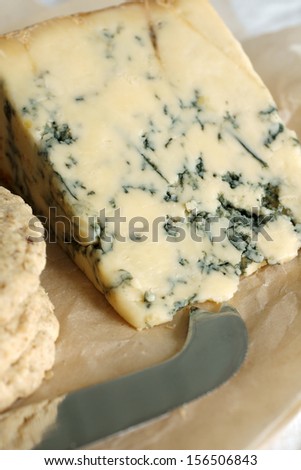 Stilton cheese on aged parchment paper with oat biscuits and cheese knife