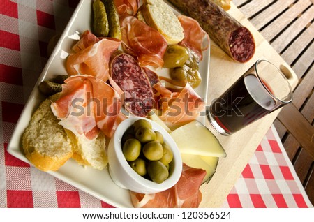 Homelike appetizer with salami, bread, olives, cheese, ham, pickles and red wine
