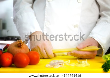 Vegetables on cutting board and chef hands with pasta, restaurant kitchen on background