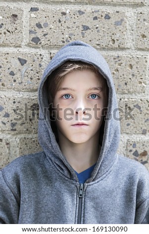 portrait of a teenage boy with grey hoodie sweatshirts standing in front of a wall.