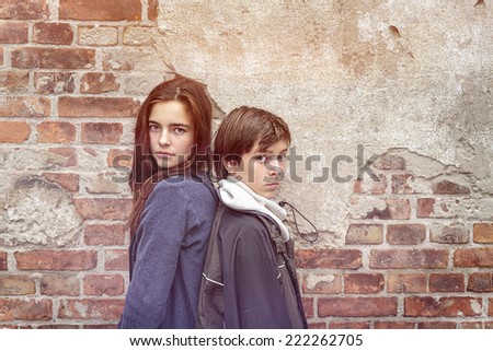 siblings back to back in front of an old brick wall
