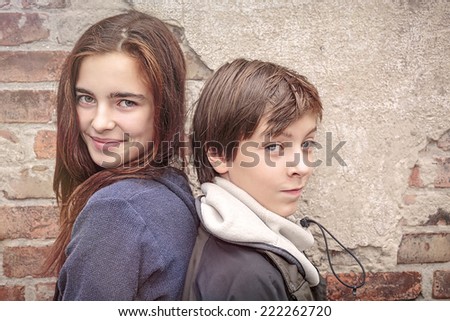 siblings back to back in front of an old brick wall