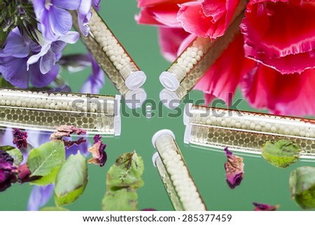 small glass tubes with homeopathy globules and flowers, laying on a mirror