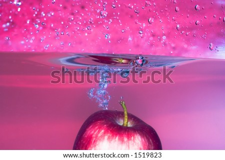 Red apple splashing into water with red background, lovely soft colour. Many drops and wet photografer after that serie :-)