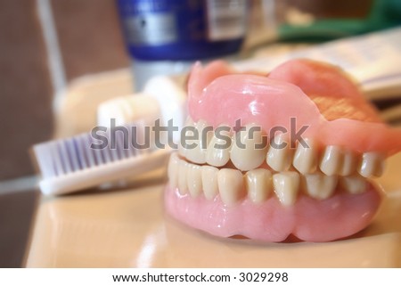 An artificial denture of a senior in a glass of water with toothbrush and paste aside. Shallow depth of field and a bit of blur motion due to lightning technique. Sharp Focus on the teeth.