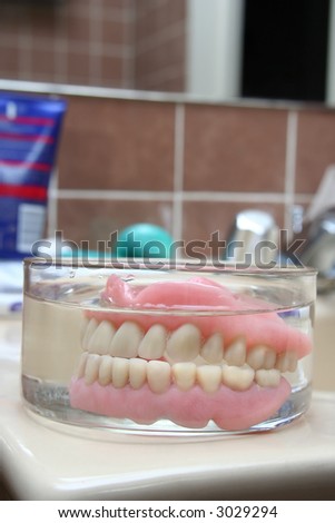 Kind of scary, isn´t it? :-)... an artificial denture of a senior in a glass of water in the bathroom. Shallow depth of field. Focus on the teeth.
