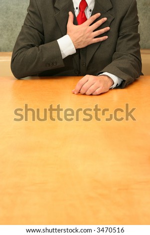 Business-man sitting at the desk, hands to his heart.