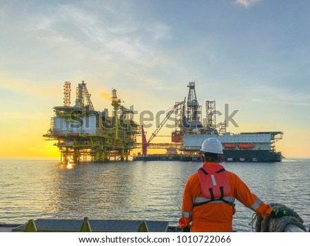 Oil and gas industry. Marine crew standing on supply vessel looking oil and gas platform during sunrise.