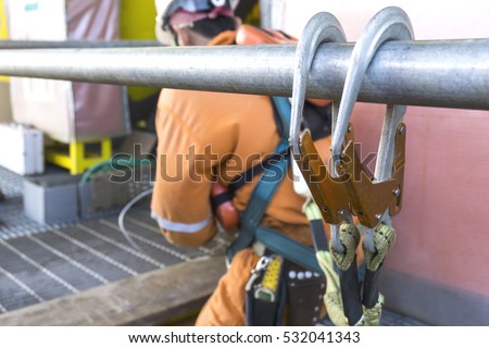 Working at height equipment. Fall arrestor device for worker with double hooks for safety body harness on selective focus. Worker as a background.
