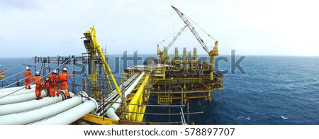 Oil and gas industries. Panorama view of offshore scaffolders standing on the pipeline and new oil and gas platform installed in the middle of the sea with cloudy sky background.