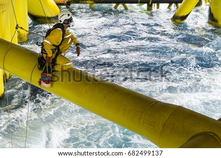 Working at height. A commercial abseiler with respiratory protection and fall arrestor device sitting on oil and gas jacket module for doing some maintenance work in the middle of the sea.
