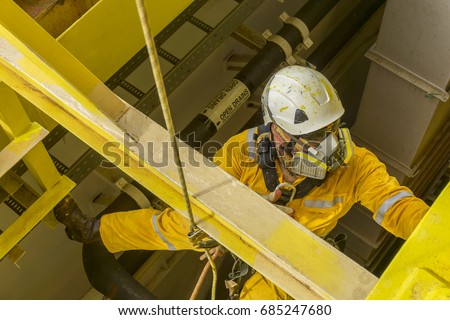 Working at height. A commercial abseiler with respiratory protection and fall arrestor device doing painting inspection on oil and gas structure platform.