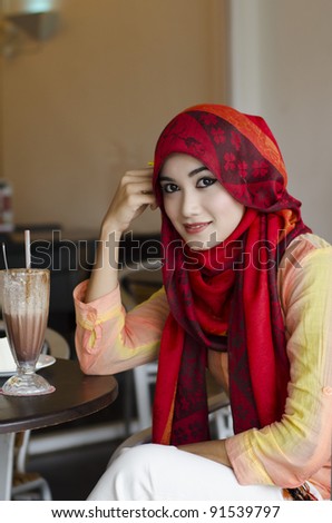 beautiful young muslim woman with stylish scarf smiling and enjoy chocolate drink in the coffee shop