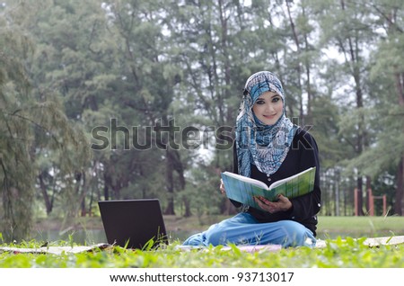 beautiful young muslimah woman with head scarf relax while reading a book at the recreation park