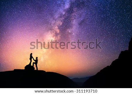 Romantic couple standing together holding hands in the mountains. Beautiful Milky Way galaxy on the background.