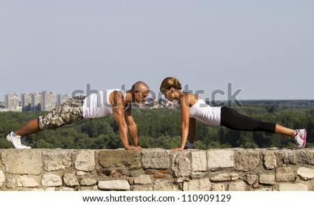 Fitness instructors doing pushups on an old stone wall. Beatiful view in bacground