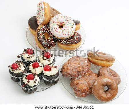 Donuts, cupcakes, and apple fritters on plates with a white background.