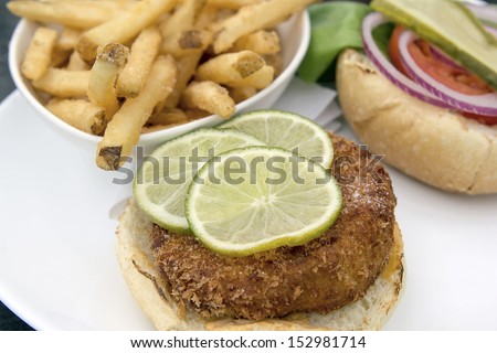 Crabcake Burger Open Face with Pickle Onion Tomato Lettuce Lemon Slices and French Fries Closeup Macro
