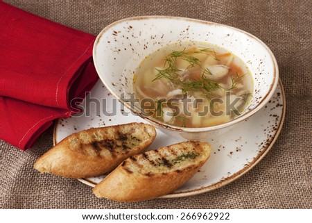 A chicken broth in white ware on burlap tablecloth