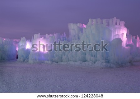 Ice structure illuminated with pink lights behind ice walls and layers of icicles