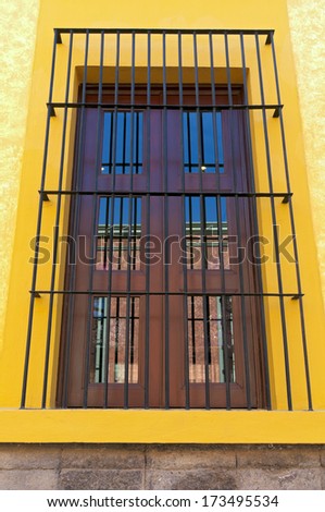 Window opening with reflections on panes surrounded by protective bars and colorful frame