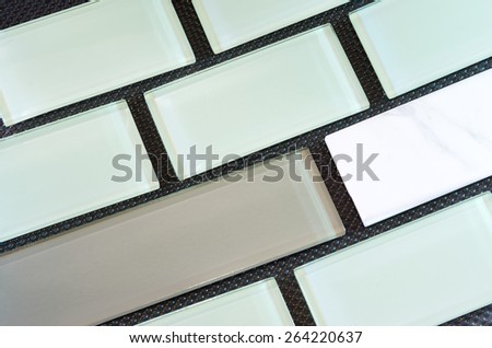 green white and taupe colored glass and porcelain subway tile or backsplash against black background arranged in rows