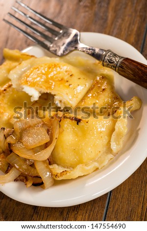 A plate of handmade pierogi with a side of carmelized onions.  There is a decorative silver and wood fork on the plate.  Everything is shot on a wood table.